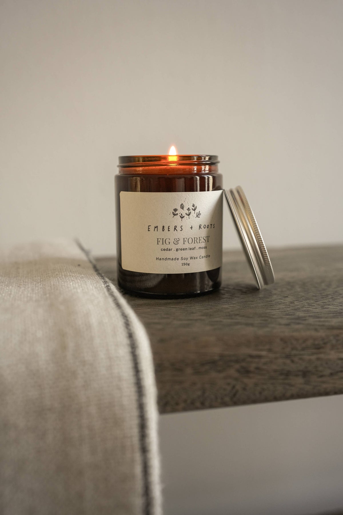 Lit Embers & Roots candle in an amber glass jar