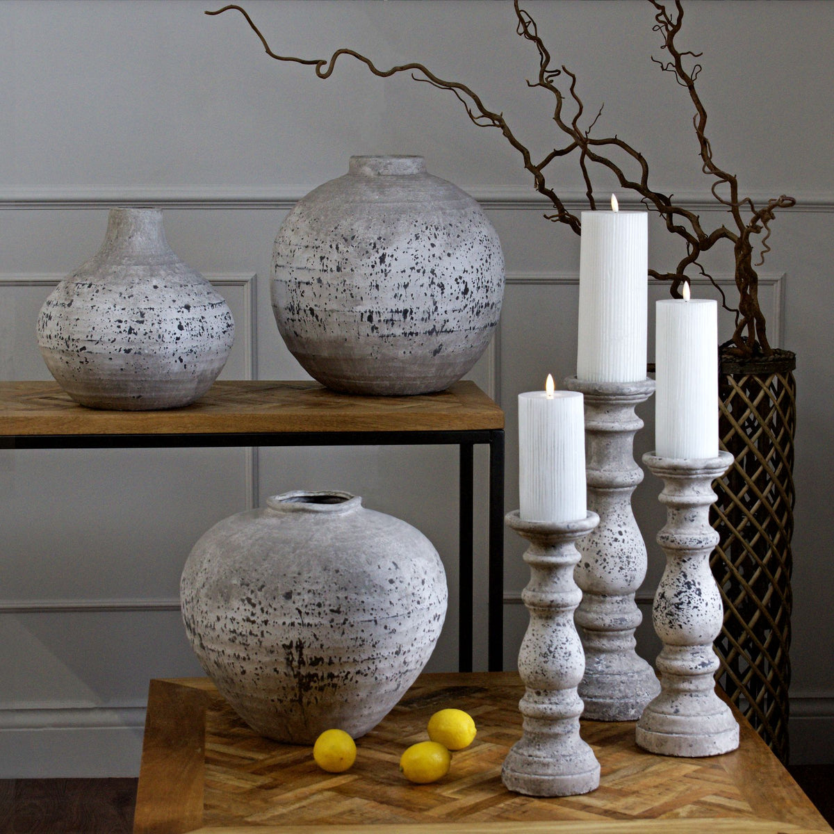 Decorative setting with speckled vases, candles, and lemons on a wooden surface.