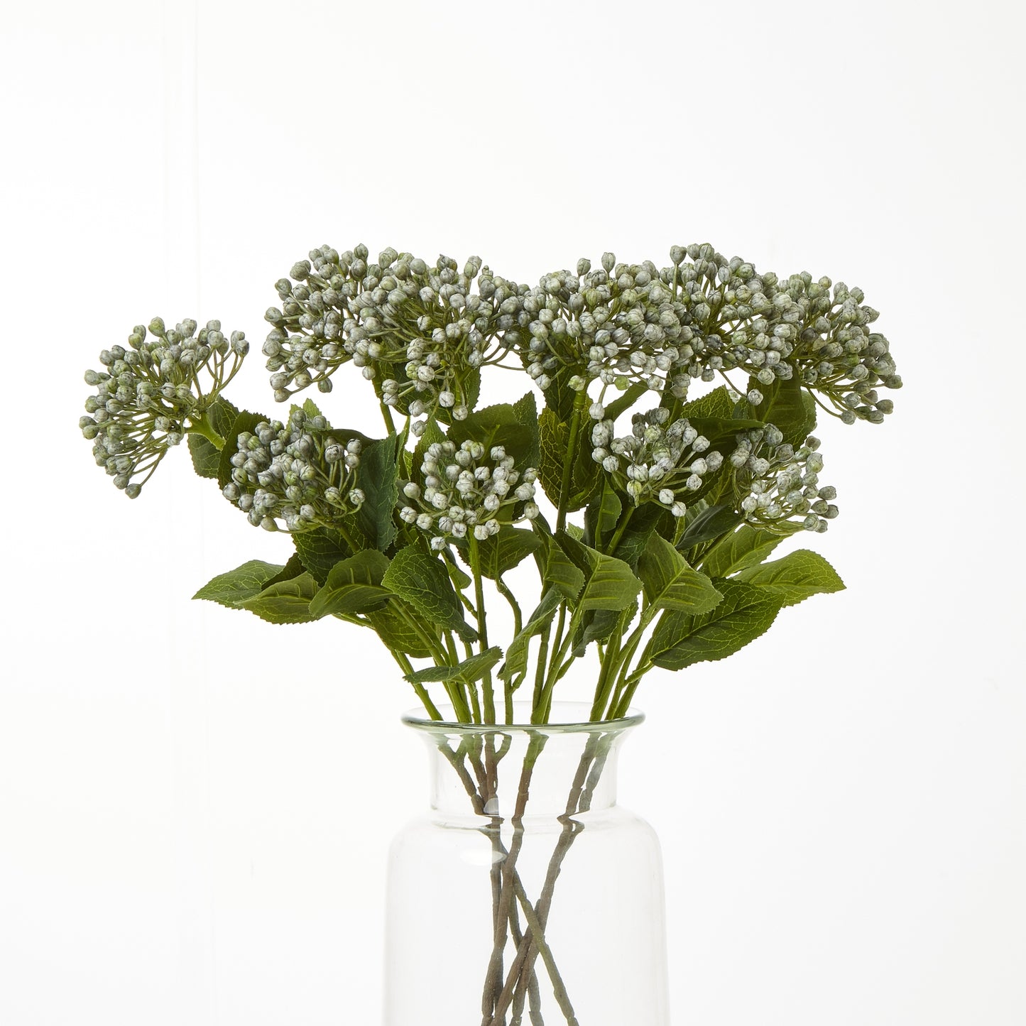 Artificial flower arrangement with green leaves and white flowers in a clear glass vase on a white background