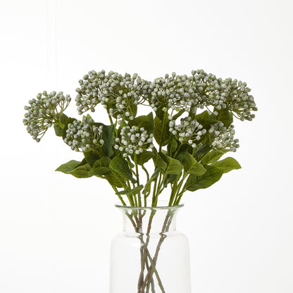 Artificial flower arrangement with green leaves and white flowers in a clear glass vase on a white background