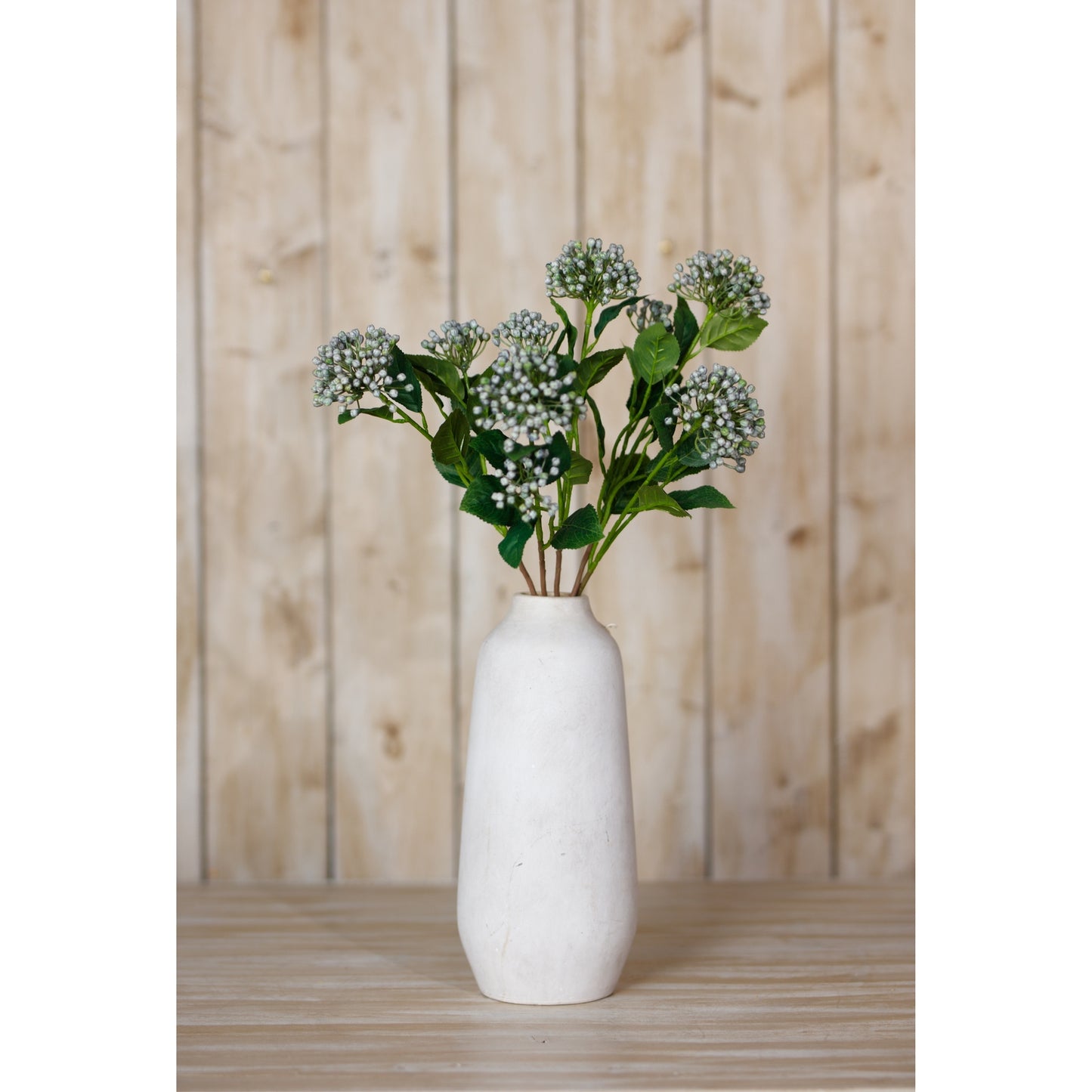 White vase with green flowers against a wooden background