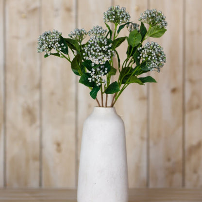 White vase with greenery against a wooden background