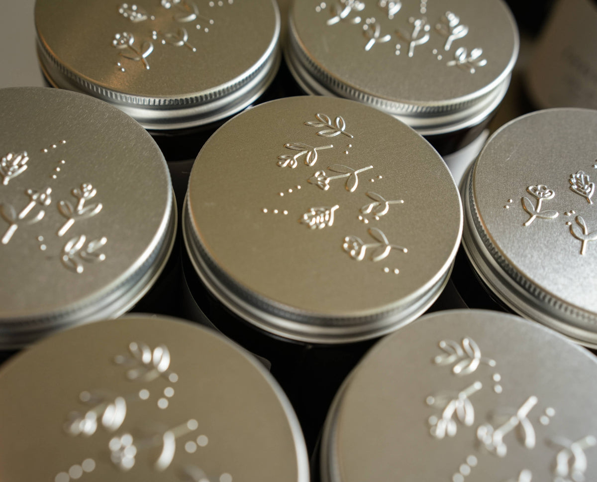 Close-up of embossed silver lids on Embers & Roots candle jars