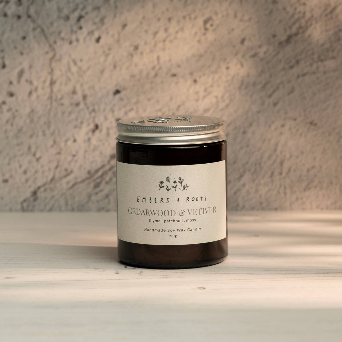 Embers & Roots Cedarwood & Vetiver soy candle in an amber glass jar with silver lid