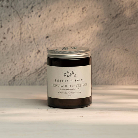 Embers & Roots Cedarwood & Vetiver soy candle in an amber glass jar with silver lid
