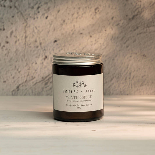 Embers & Roots Winter Spice soy candle in an amber glass jar with silver lid