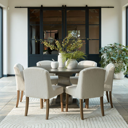 Dining room with a round table and chairs, plants, and sliding glass doors.