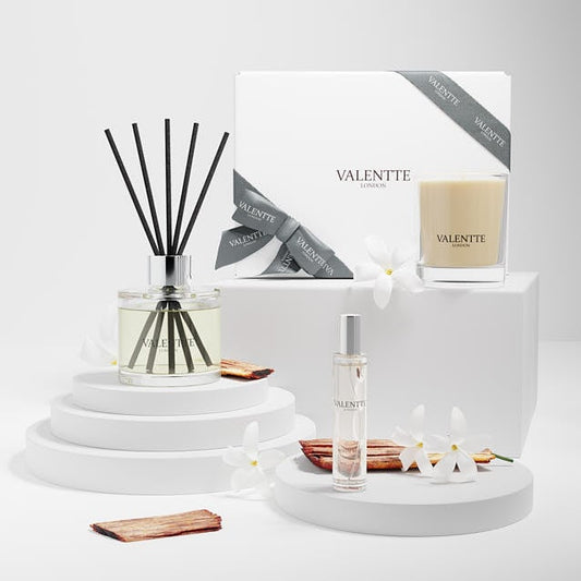 Valentte London gift set featuring a reed diffuser, a scented candle, and a perfume bottle, styled on white pedestals with white flowers and cinnamon sticks.