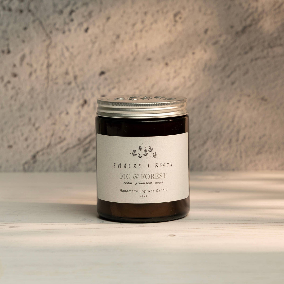 Embers & Roots Fig & Forest soy candle in an amber glass jar with silver lid